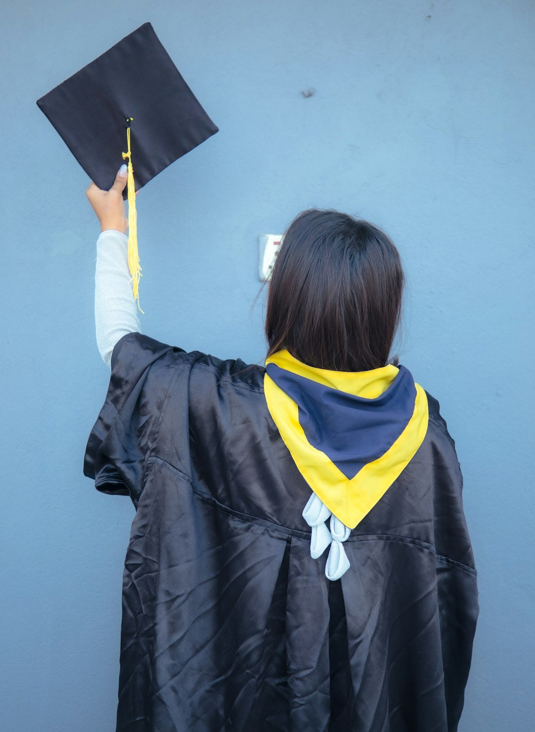 a woman in a graduation gown holding up a black graduation hat
